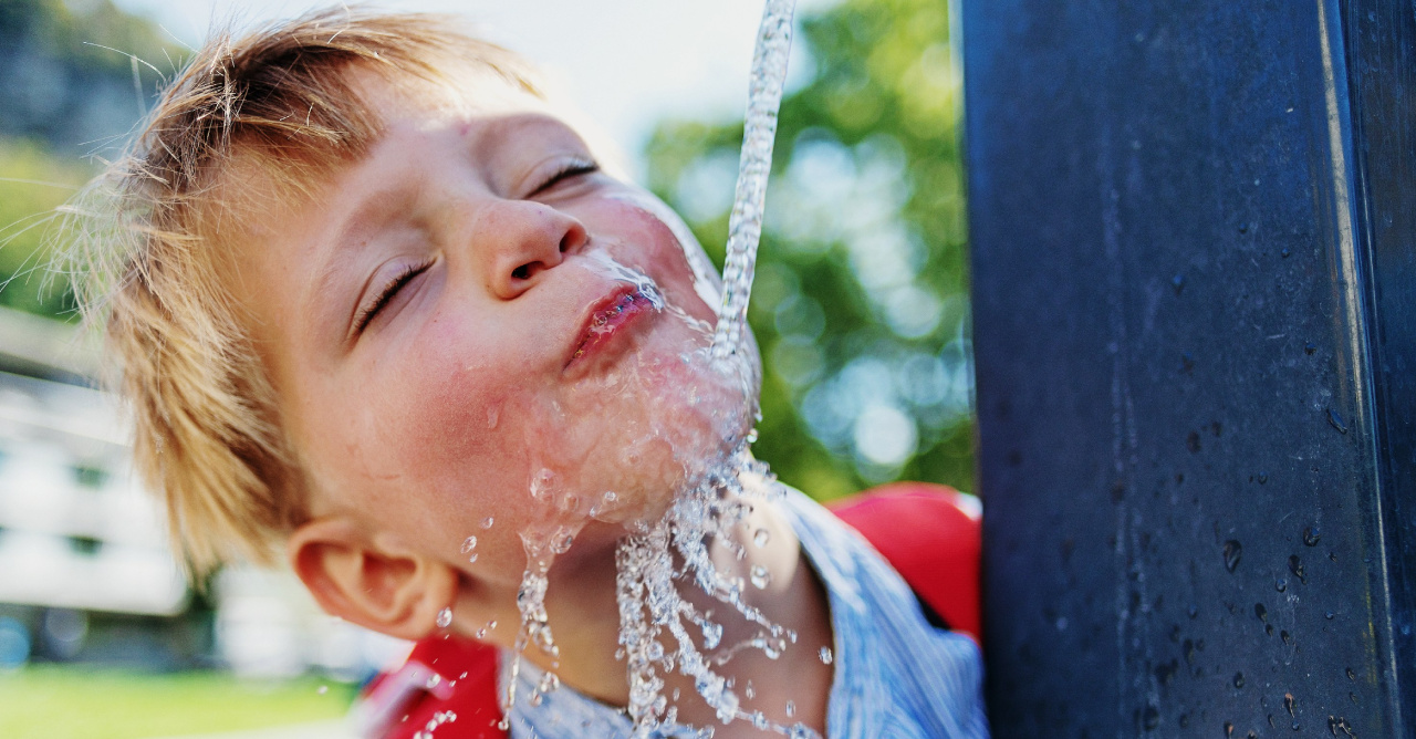Junge, der an einem Brunnen Wasser trinkt