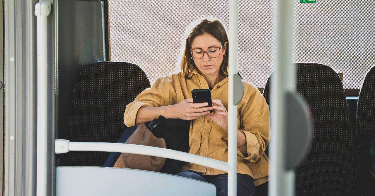 Eine Frau sitzt in einem Bus und blickt auf ihr Handy.