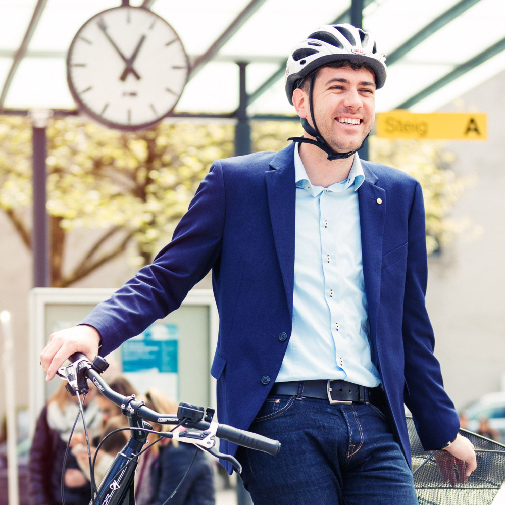 Ein Mann mit Fahrradhelm lehnt an der Bushaltestelle auf seinem Fahrrad.