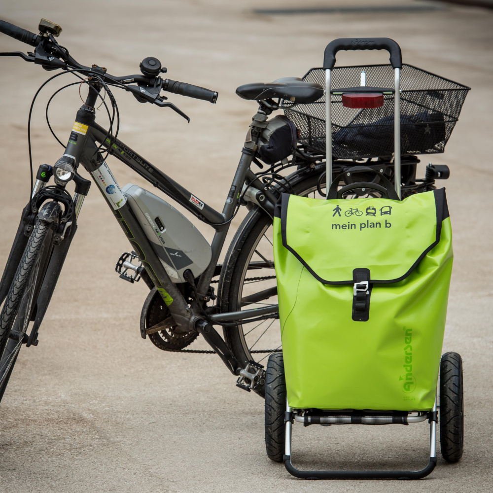 Ein schwarzes Fahrrad auf Asphalt, daneben steht ein grüner Fahrrad-Trolley mit plan b-Logo