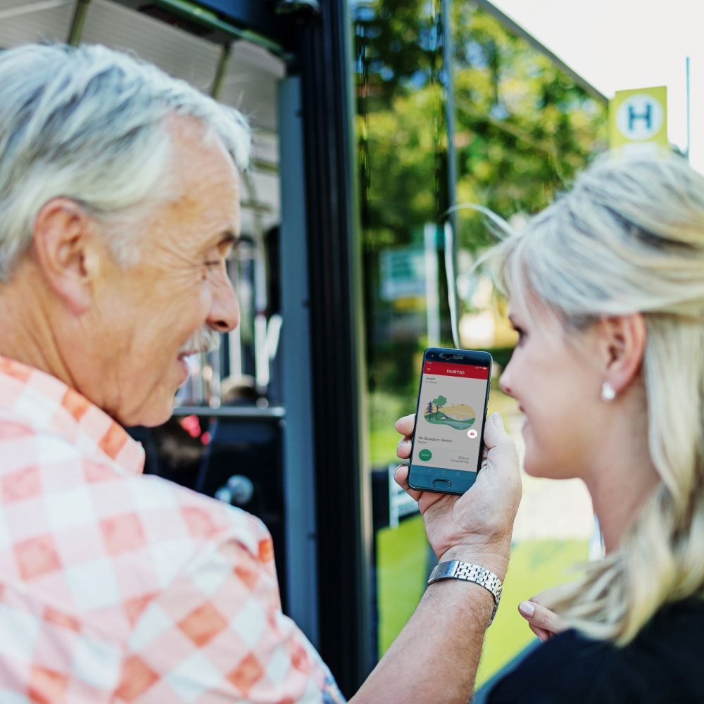 Zwei Personen sind von hinten zu sehen, wie sie vor einem Bus stehen und ein Handy halten.