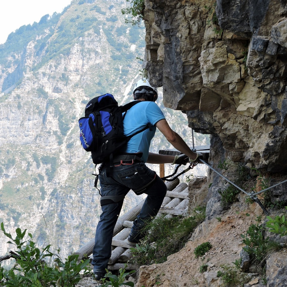Ein Mann klettert an einem Stahlseil gesichert um einen Felsen.