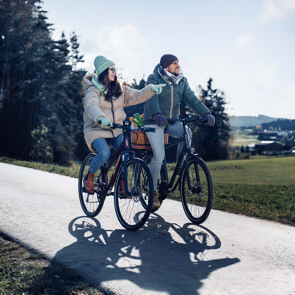 Eine Frau und ein Mann in Winterkleidung radeln nebeneinander auf einem Radweg.