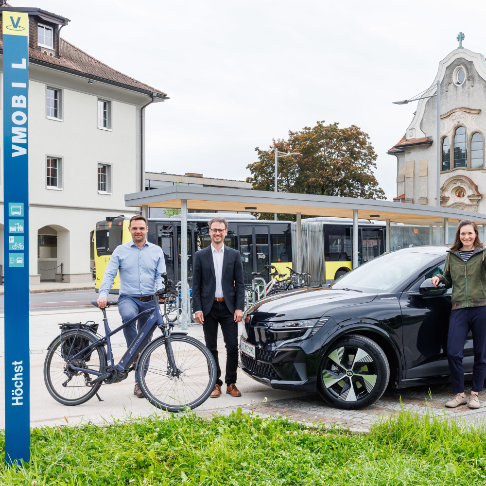 VMOBIL Station am Kirchplatz in Höchst mit Bürgermeister, Landesrat und Projektleiterin mit Bus, carsharing Auto und Rad im Bild