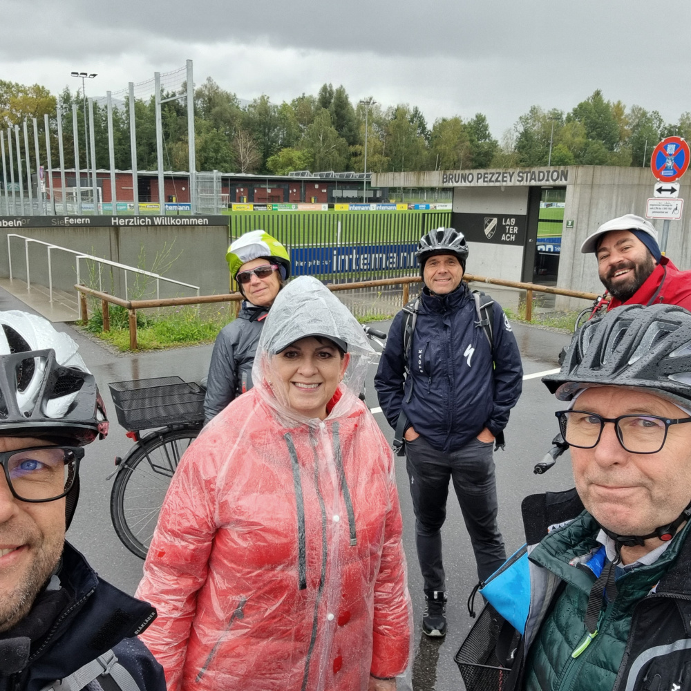 Gruppenfoto mit Vize-Bürgermeisterin Sabine Kassegger die mit einer Gruppe in der Region im Zuge einer Radexkursion unterwegs ist. Sie stehen hier vor dem Bruno-Pezzey-Stadion in Lauterach.