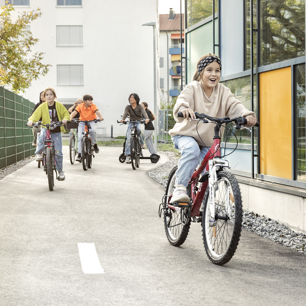 Eine Gruppe von Kindern fährt Fahrrad. Ein junges Mädchen ist im Vordergrund, die restlichen Kinder folgen ihr weiter hinten. 