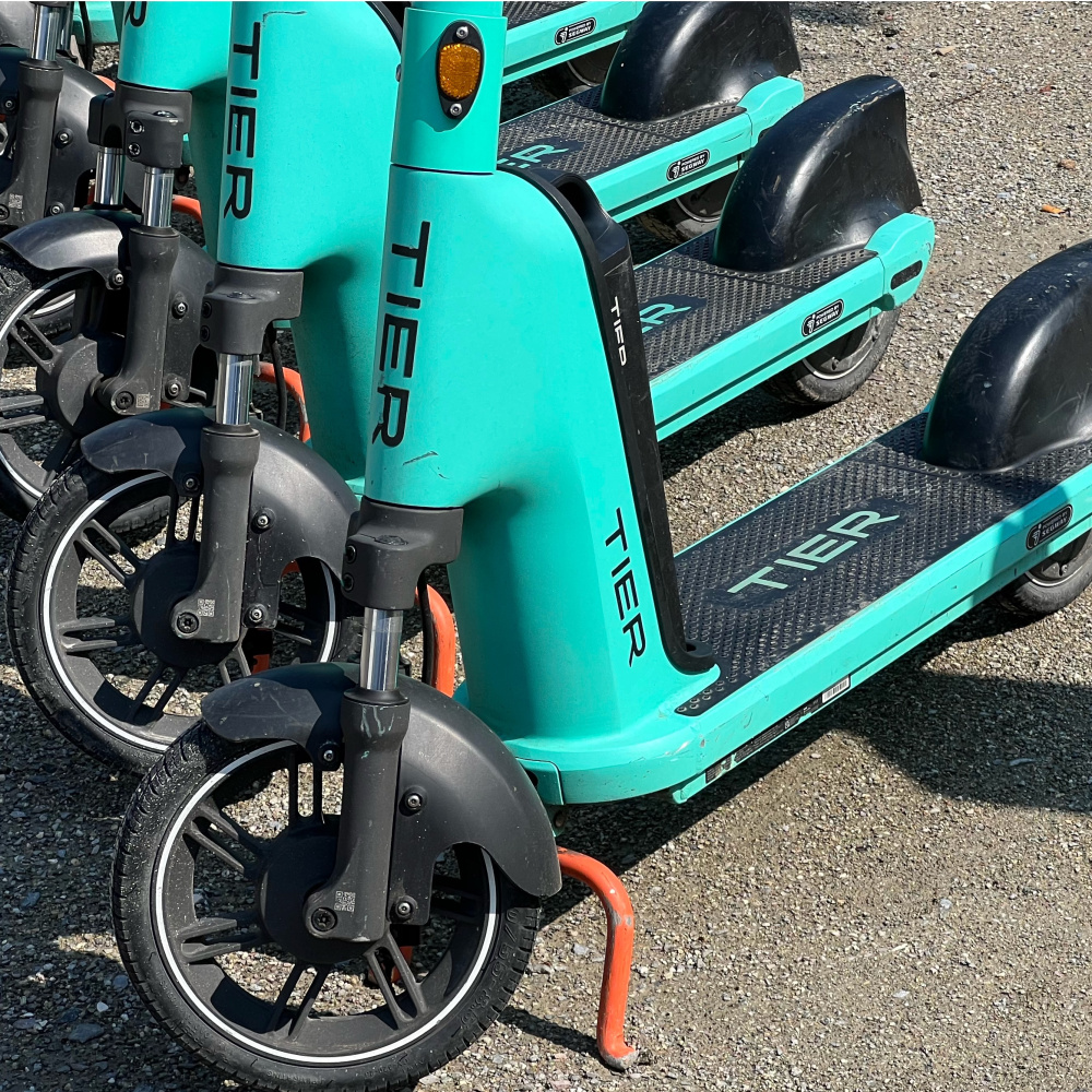 Mehrere türkise Leih-E-Scooter stehen geparkt auf dem Asphalt nebeneinander