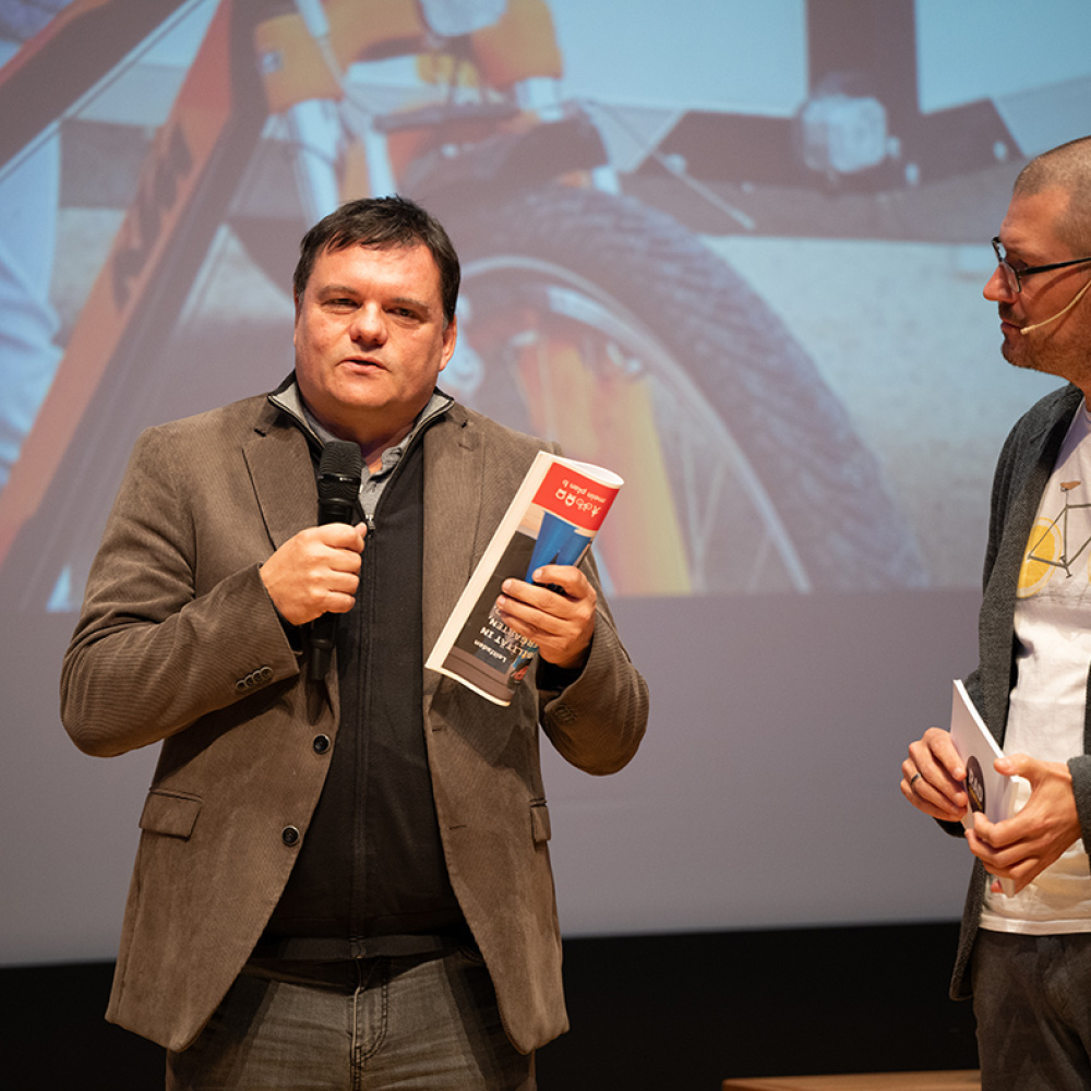 Bürgermeister Thomas Schierle präsentiert auf der Bühne die plan b-Region. Daneben der Moderator. 