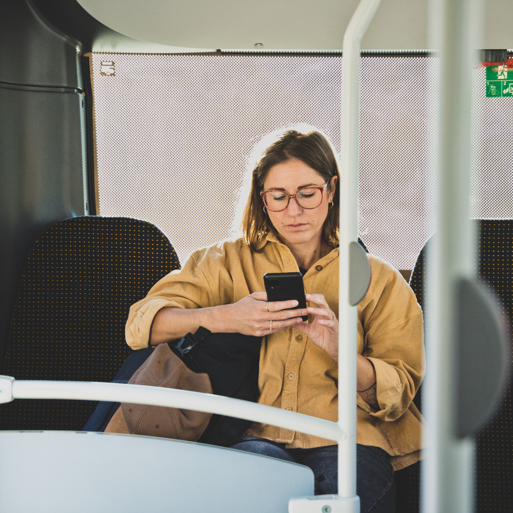 Eine Frau sitzt in einem Bus und blickt auf ihr Handy.