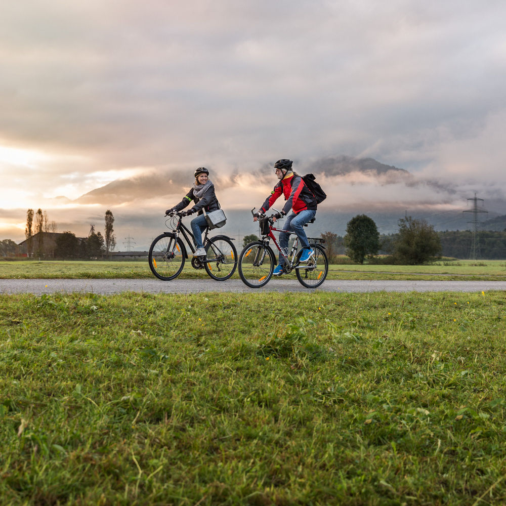 Eine Frau und ein Mann radeln gemeinsam durch eine herbstliche Landschaft.