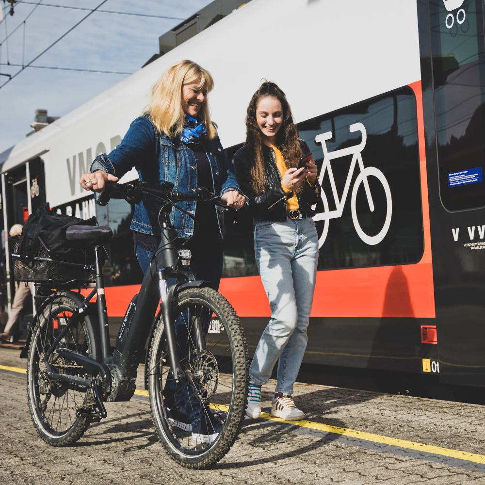 Ein Fahrgast mit Rad und eine Frau mit Handy am Bahnsteig kurz vor dem Einsteigen in den Zug.