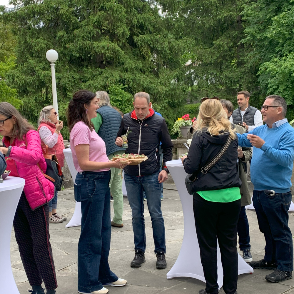 Teilnehmer:innen der Fahrradgenusstour genießen an Stehtischen im Freien das Menü