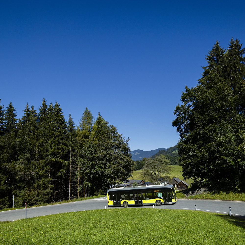 Ein E-Bus fährt auf einer Bergstraße mit einem Wald im Hintergrund.