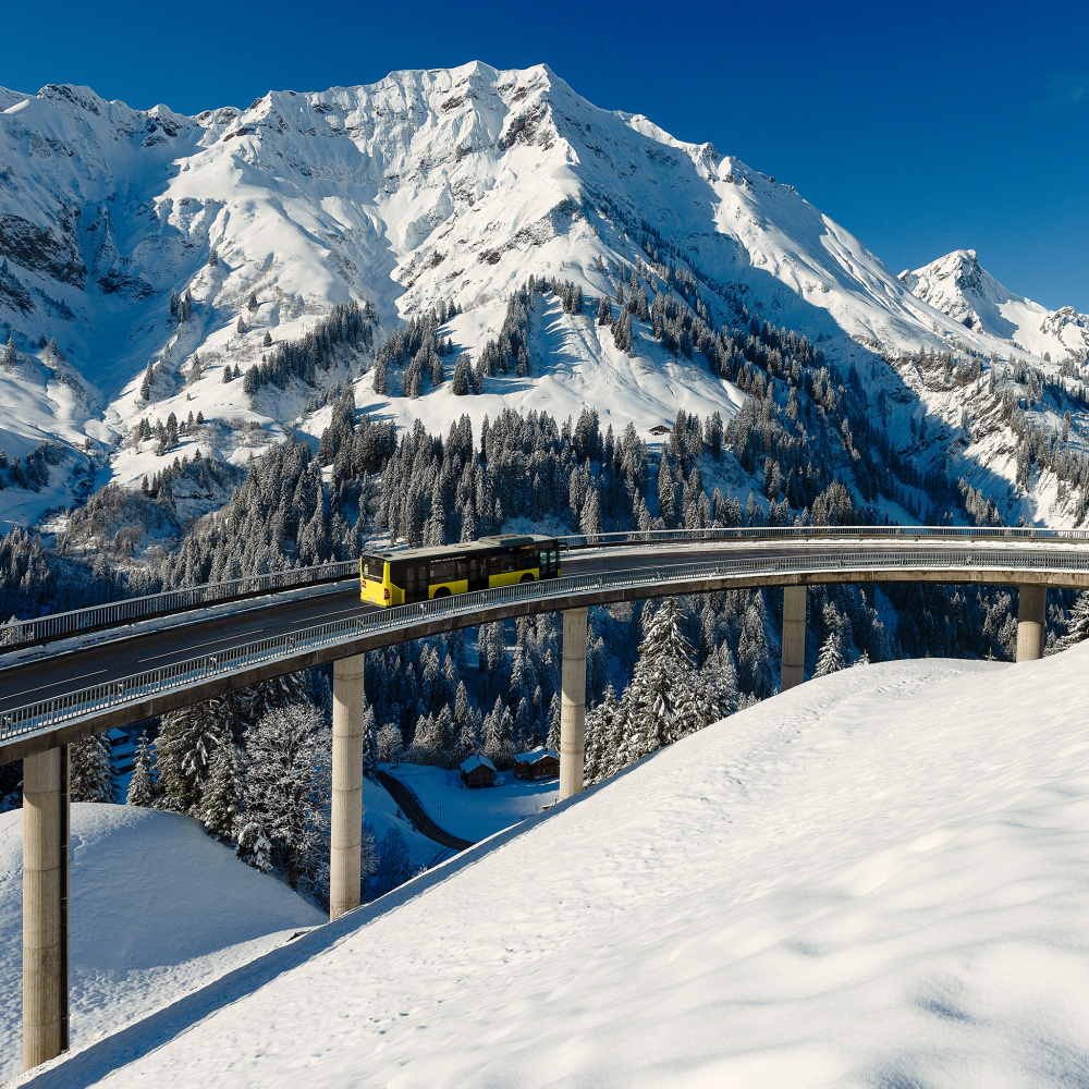 Ein Bus unterwegs in der verschneiten Winterlandschaft in den Bergen Vorarlbergs. 