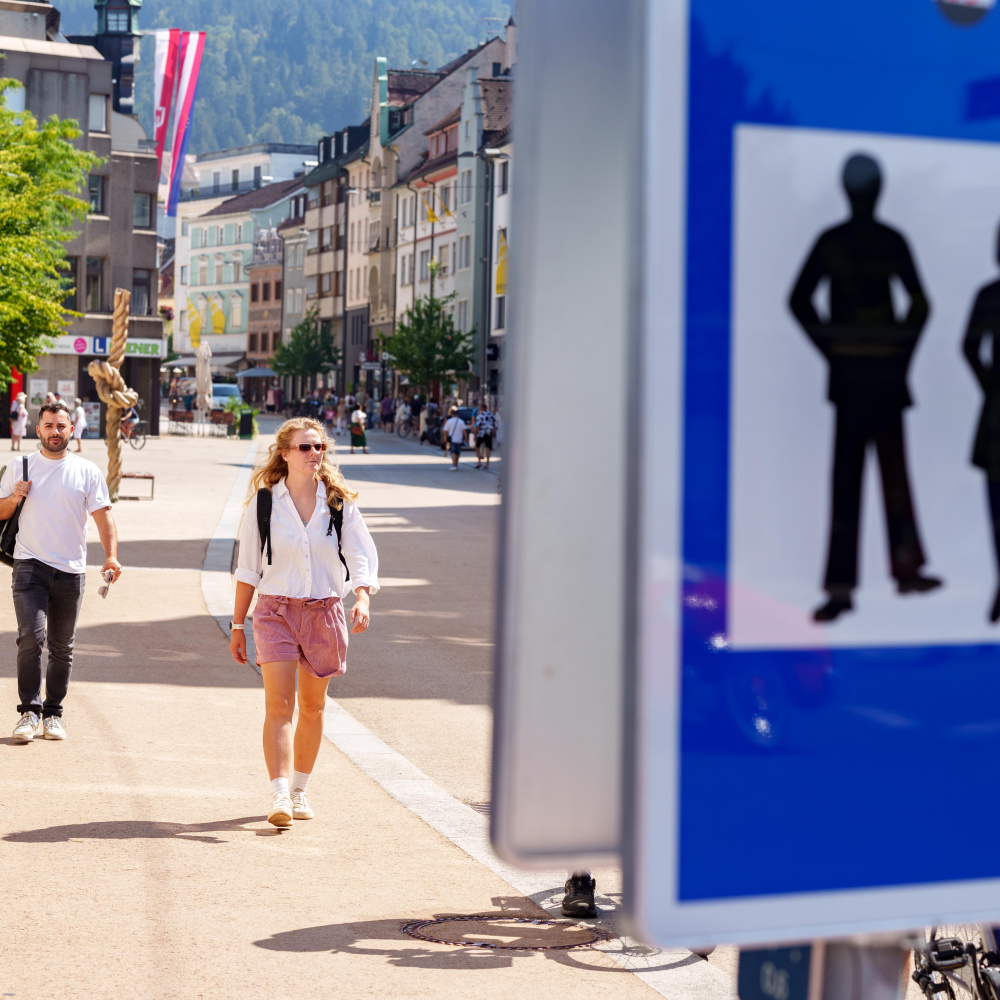 Fußgängerzone-Schild im Vordergrund, dahinter belebte Innenstadt mit Passanten