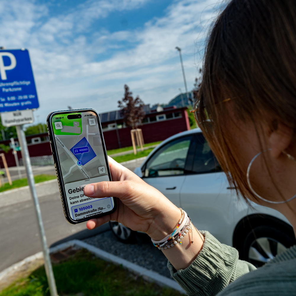 Person parkt per Handy ihr Fahrzeug an einem ausgeschilderten Platz. 