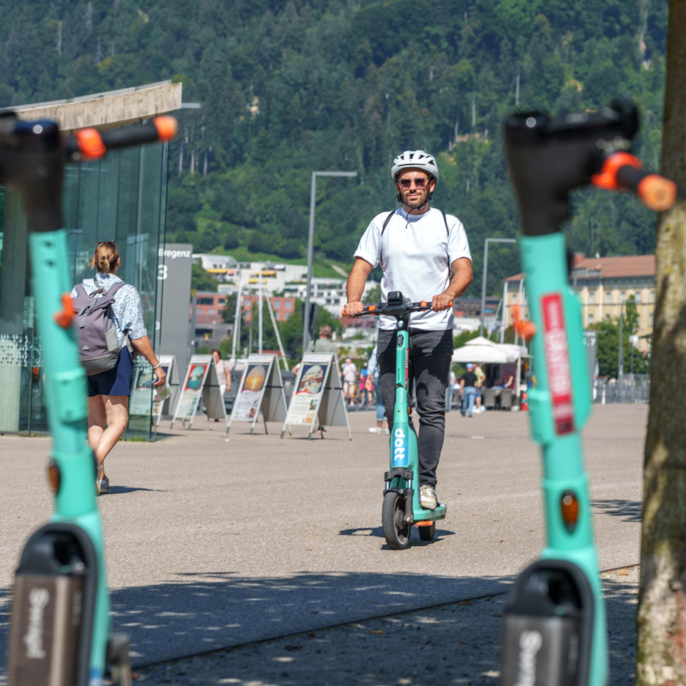 Mann mit Helm ist mit einem türkisen E-Scooter von "Dott" in Bregenz unterwegs.