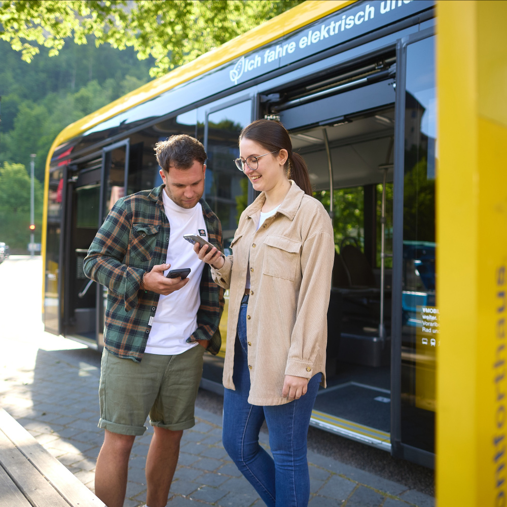 Personen stehen vor einem Bus und schauen etwas am Handy nach