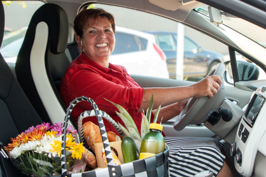 Frau sitzt im Carsharing-Auto mit ihrem Einkauf auf dem Beifahrersitz.