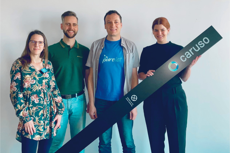Mitglieder vom Verein pure und Mitarbeiterin von caruso carsharing halten eine Stele von caruso carsharing.