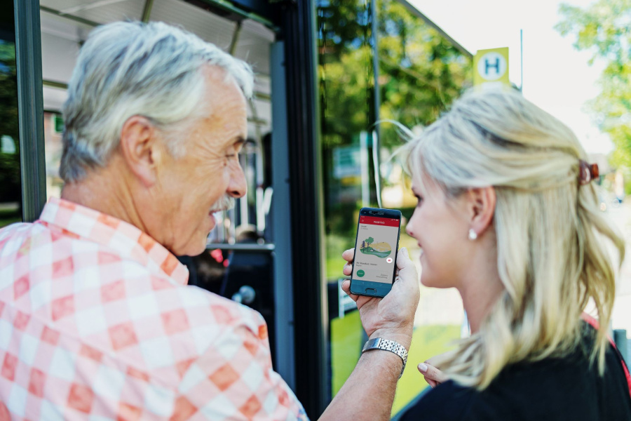 Zwei Personen sind von hinten zu sehen, wie sie vor einem Bus stehen und ein Handy halten.