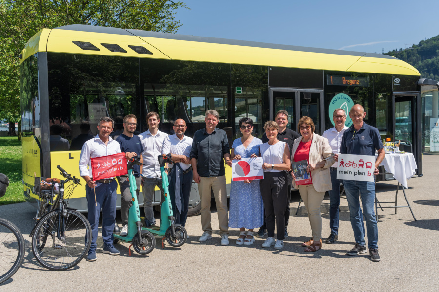 Vertreter:innen der plan b-Gemeinden stehen mit E-Scootern, Fahrrädern und Plakaten zu plan b vor einem E-Bus des Landbus Unterland bei schönem Wetter beim Platz der Menschenrechte in Bregenz