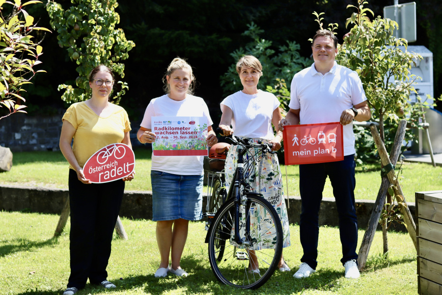Gruppenbild mit Irina Antlinger mit dem "Österreich radelt"-Schild, Julie Buschbaum mit dem "Radkilometer wachsen lassen"-Sujet, Bgmin. Angelika Moosbrugger mit dem Fahrrad und Bgm. Thomas Schierle mit der plan b-Fahne. Sie mit dem Sujet zur Aktion "Radkilometer wachsen lassen" ein