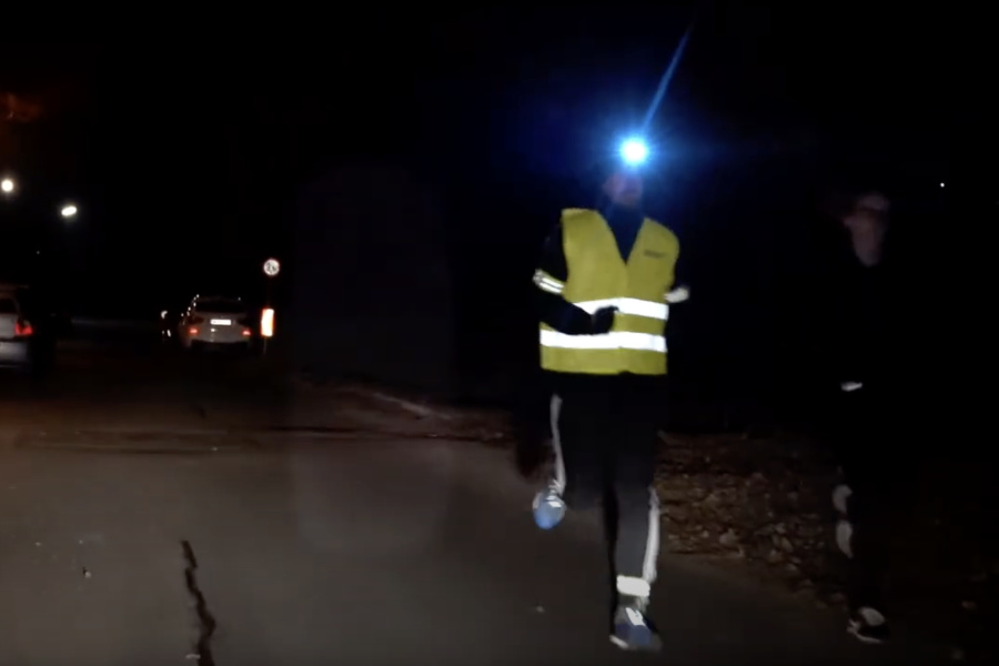 Eine Person joggt in der Dunkelheit und macht sich mit Warnweste, Stirnlampe und Refelektorbändern sichtbar.