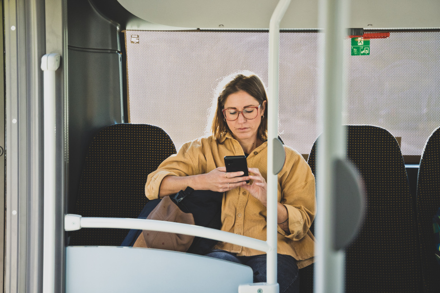 Eine Frau sitzt in einem Bus und blickt auf ihr Handy.