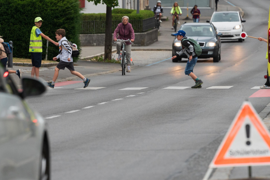 Schüler überqueren auf dem Weg zur Schule einen Zebrastreifen. Schülerlotsen sorgen für Sicherheit und stoppen die Autos.