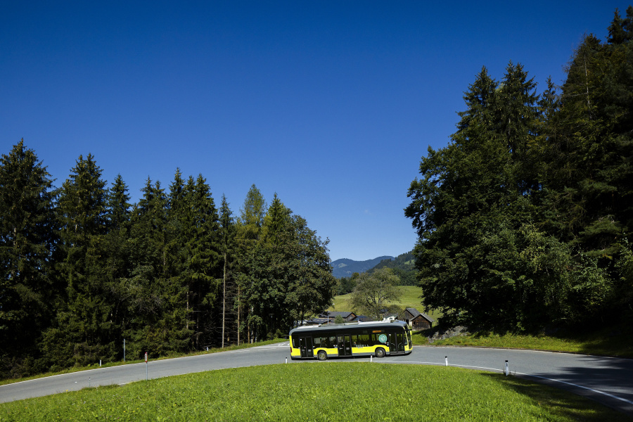 Ein E-Bus fährt auf einer Bergstraße mit einem Wald im Hintergrund.