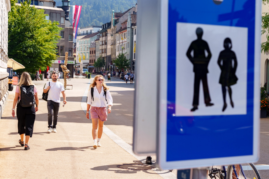 Fußgängerzone-Schild im Vordergrund, dahinter belebte Innenstadt mit Passanten