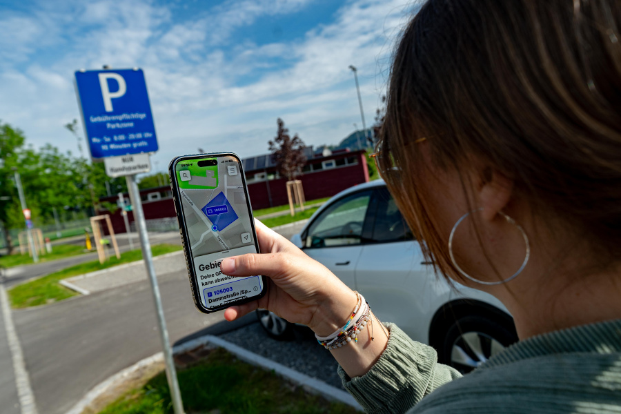 Person parkt per Handy ihr Fahrzeug an einem ausgeschilderten Platz. 