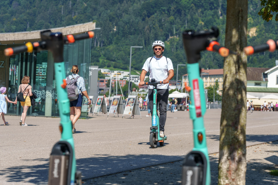Mann mit Helm ist mit einem türkisen E-Scooter von "Dott" in Bregenz unterwegs.