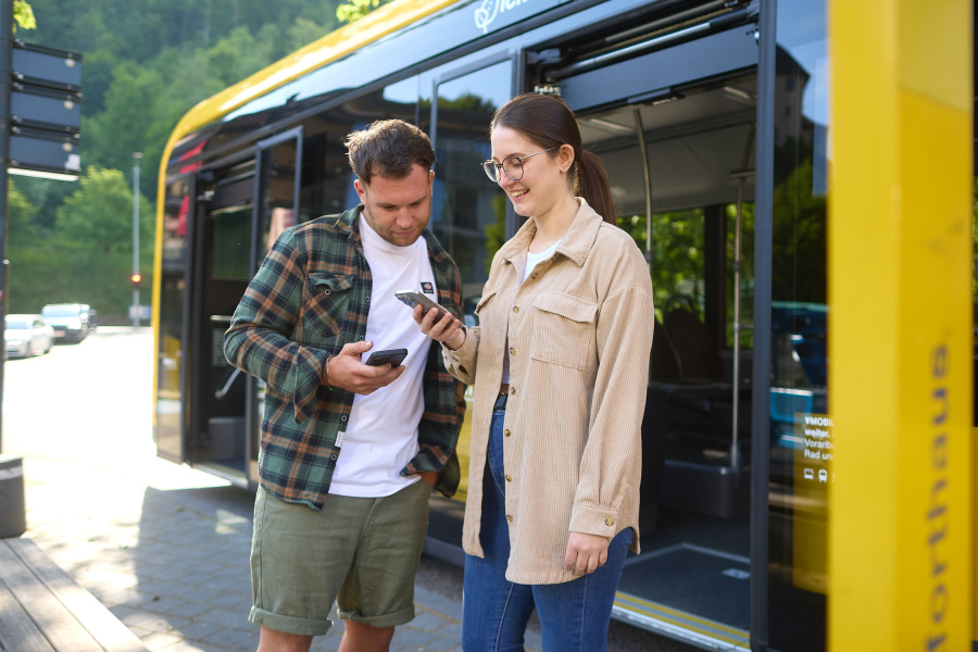 Personen stehen vor einem Bus und schauen etwas am Handy nach